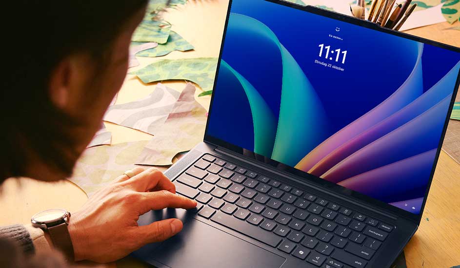 Een laptop staat open op een bureau, met een blauw scherm dat 11:11 toont. De hand typt op het toetsenbord.