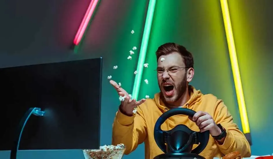 Un écran noir, un volant et du pop-corn sont visibles. Des néons roses, verts et jaunes illuminent le fond.