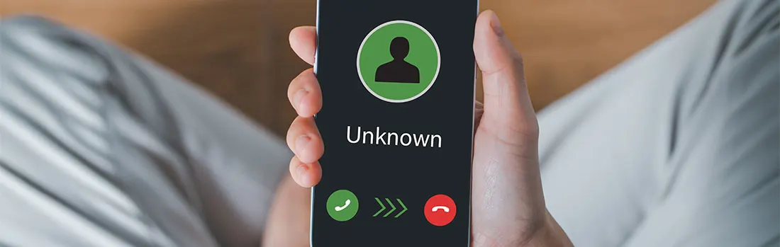 Un téléphone affiche "Inconnu" avec des icônes vertes et rouges sur un fond noir, tenu devant un pantalon gris clair.