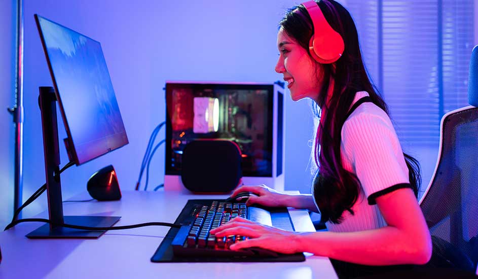 Bureau avec écran, clavier et unité centrale éclairée. Casque audio rouge sur la table. Éclairage bleu et rose.