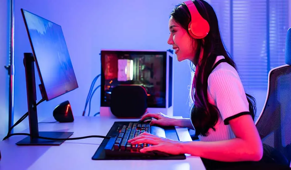 Bureau avec écran, clavier et unité centrale éclairée. Casque audio rouge sur la table. Éclairage bleu et rose.
