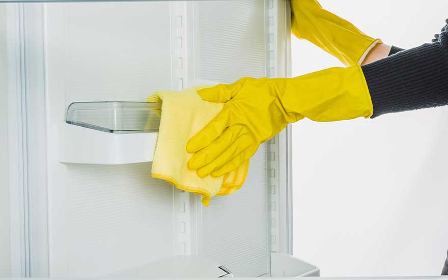 Een koelkast wordt schoongemaakt met gele handschoenen en een gele doek.