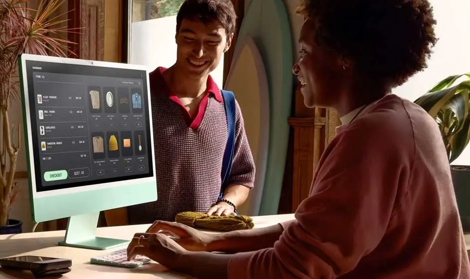 Een man en vrouw bespreken een bestelling bij een computer. Op het scherm staan productafbeeldingen en een overzicht, in een warme winkelomgeving.