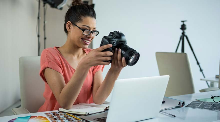 Une caméra noire tenue au-dessus d'un ordinateur portable blanc sur un bureau avec des nuanciers et un trépied.