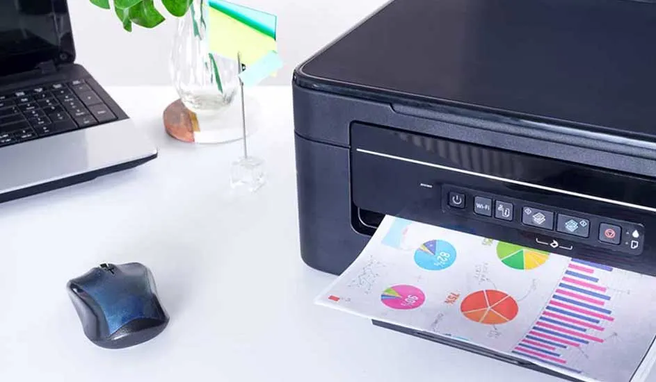 Een bureau met een zwarte printer die een pagina met cirkel- en staafdiagrammen afdrukt. Een laptop, muis en plant staan op de achtergrond.