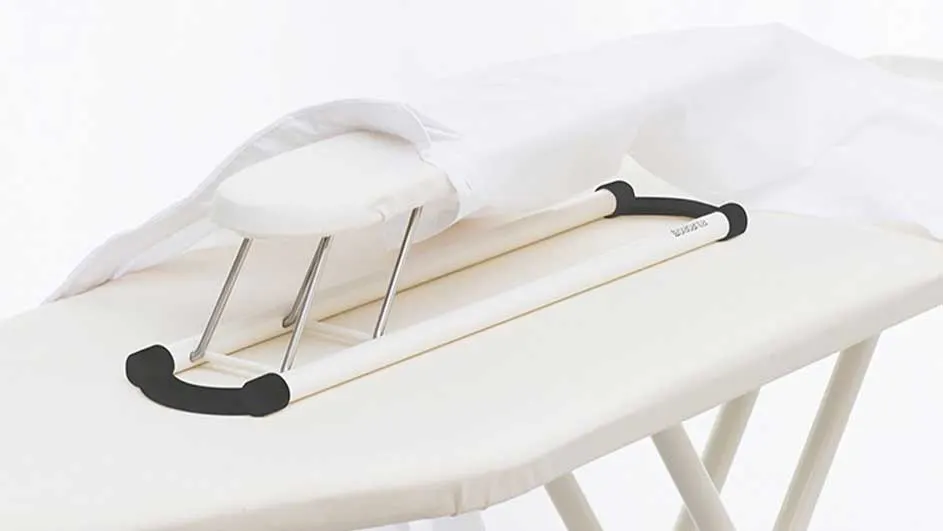 Table à repasser blanche avec repose-manches et linge blanc. Pieds en métal et extrémités noires.