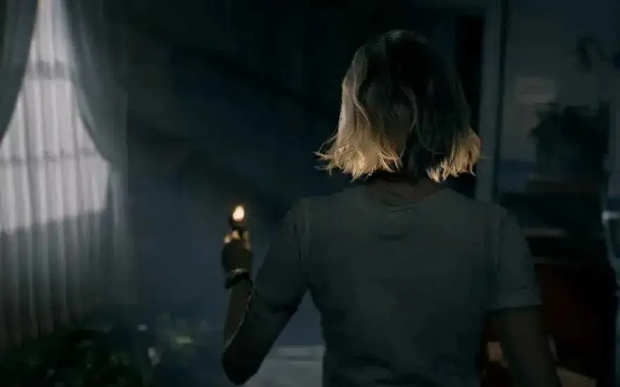 This is a video game. A short-haired blonde woman walks through a dark house holding a lighter; dim light, drifting dust, and heavy shadows.