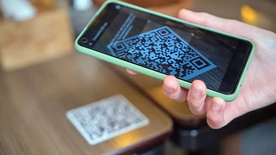 Un téléphone vert affiche un code QR. Un code QR imprimé est posé sur une table en bois clair.