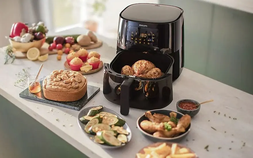 Une friteuse noire Philips montre 180 degrés. Il y a des aliments autour : des légumes, des frites et un gâteau.
