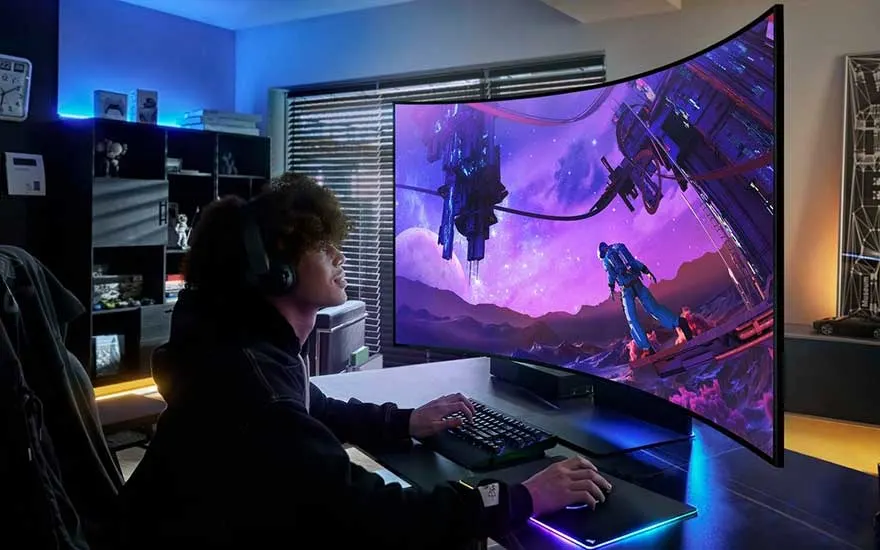 Un écran incurvé affiche un jeu vidéo violet. Un clavier et une souris sont sur un bureau noir. L'éclairage ambiant est bleu.