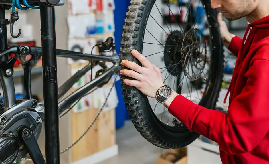 Zwarte fiets in een reparatiestandaard, met een hand op de band en een horloge om de pols.