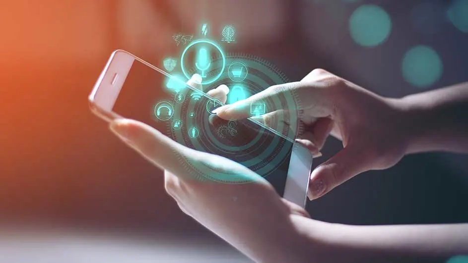 Mains tenant un smartphone blanc, avec un affichage d'icônes bleues. Le fond est flou avec des lumières.