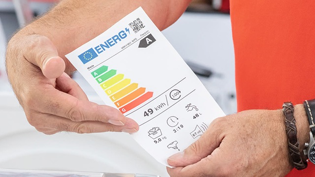 Des mains tiennent une étiquette énergie européenne indiquant la classe énergétique A, avec des informations comme la consommation, la capacité et le niveau sonore.
