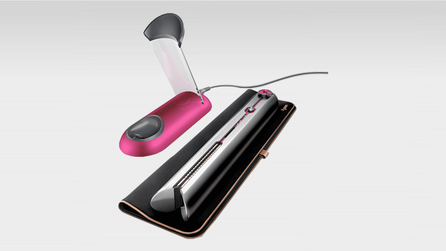 Een roze föhn en een zilveren stijltang rusten op een zwarte hittebestendige mat tegen een lichtgrijze achtergrond.