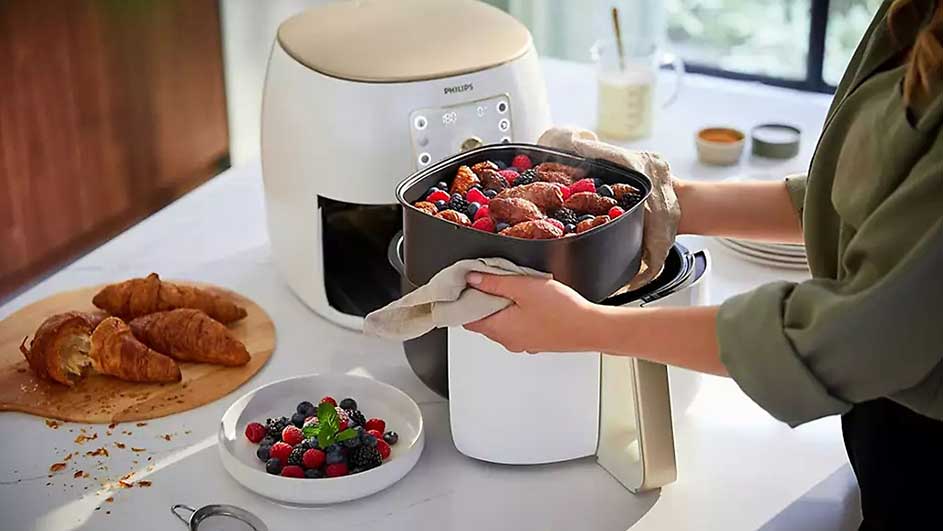 Une friteuse blanche est sur une table avec des croissants, des fruits rouges et un plat plein.