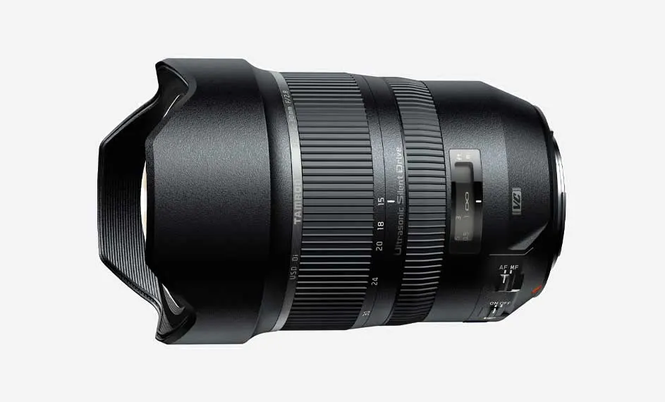 Zwarte Tamron zoomlens met ribbels en schuifregelaars, liggend op een witte achtergrond.