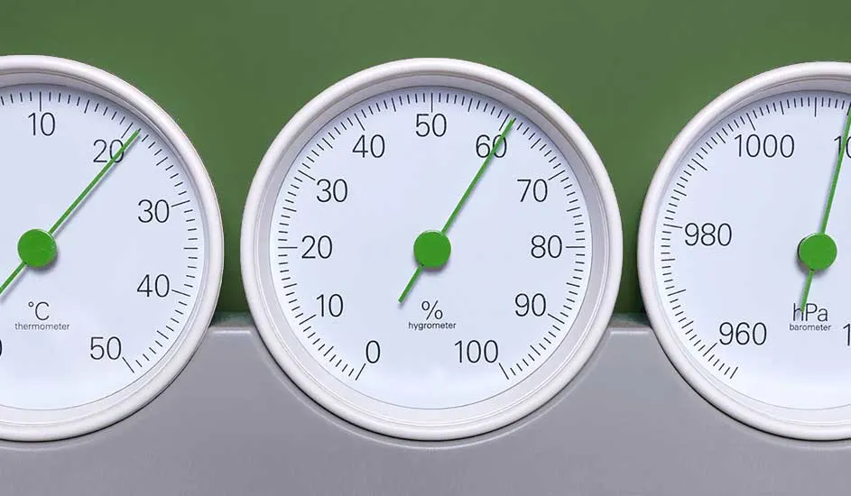 Drie witte meters met groene wijzers op een grijze ondergrond tegen een groene achtergrond. De meters tonen temperatuur, luchtvochtigheid en luchtdruk.