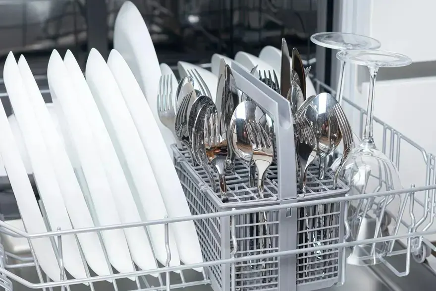 Plates, cutlery and wine glasses are clean and neatly arranged in the rack of a dishwasher. No brand is visible on the appliance.