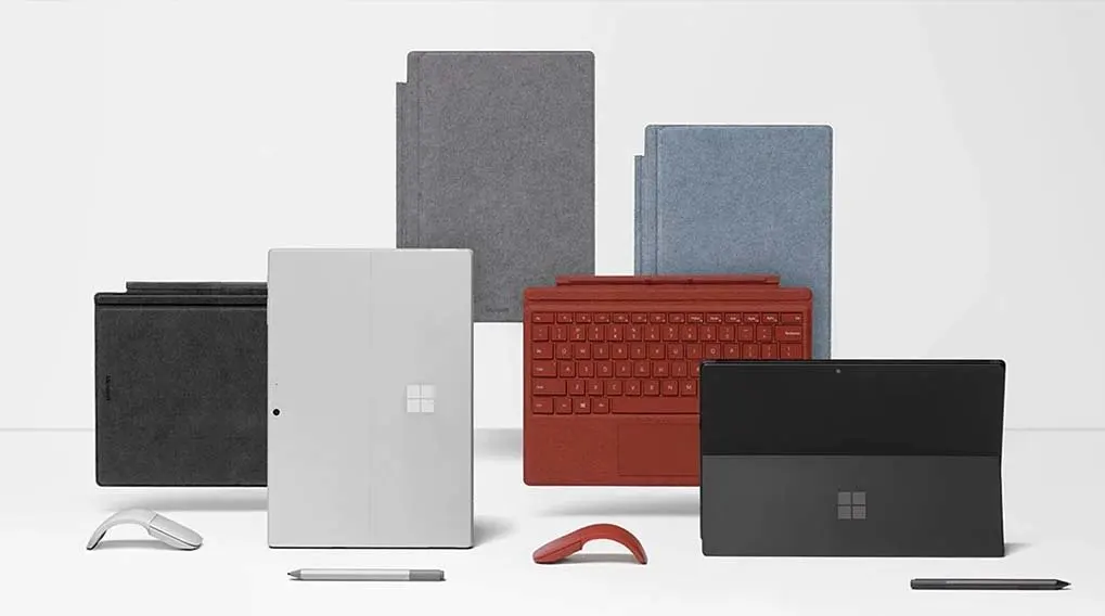 Divers appareils Microsoft : tablettes, claviers rouge et gris, souris, stylos. Fond blanc.