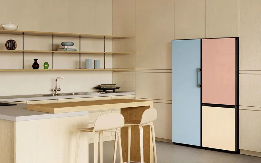 Cuisine avec réfrigérateur à panneaux bleu, rose et beige. Îlot central avec tabourets et étagères ouvertes au mur.