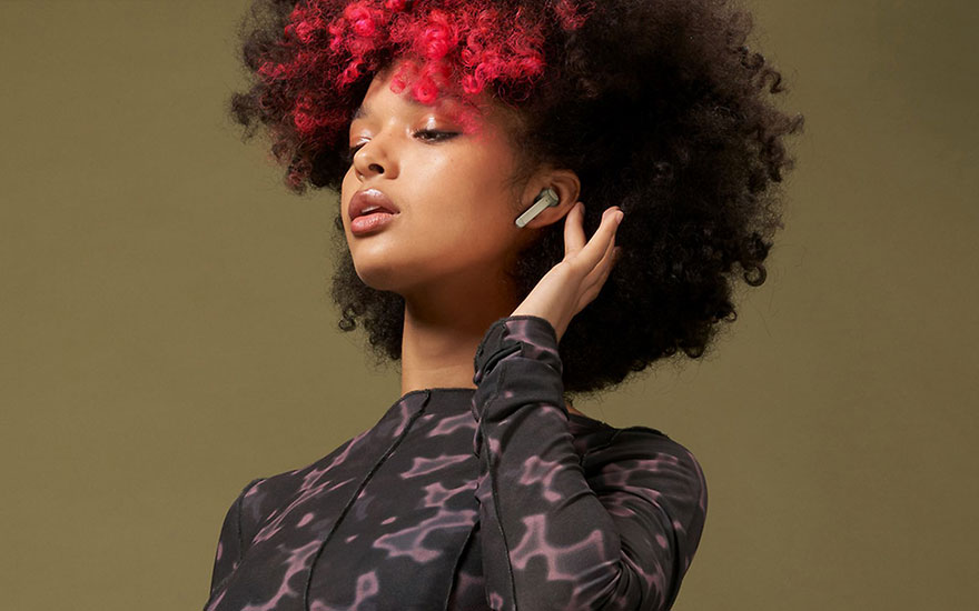 Une personne portant un écouteur sans fil. Elle porte un haut à motifs sur fond uni.