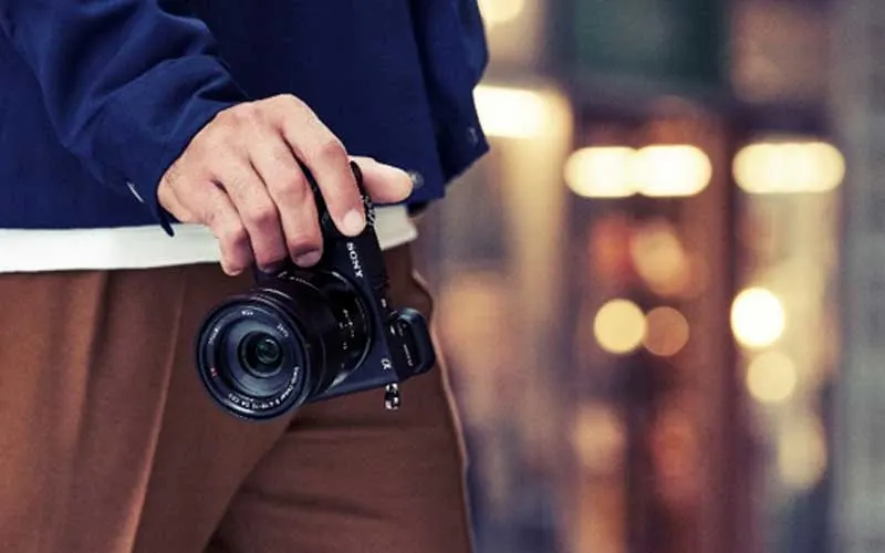Une personne tient un appareil photo compact Sony dans un environnement urbain, avec des lumières floues en arrière-plan.