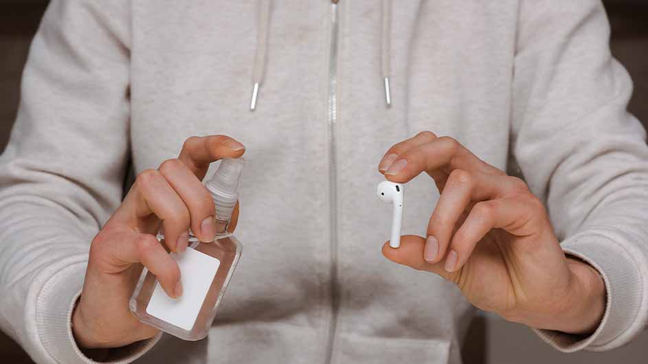 Une personne tient un désinfectant et un écouteur blanc. Le fond est un pull gris clair.