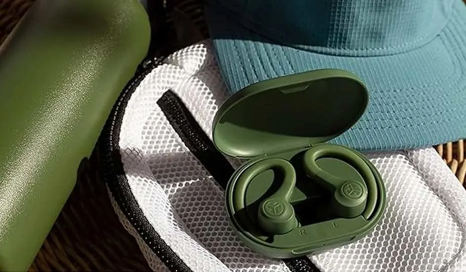 Bouteille verte, écouteurs verts dans un étui ouvert sur un sac en filet blanc et une casquette bleue, sur une surface texturée.