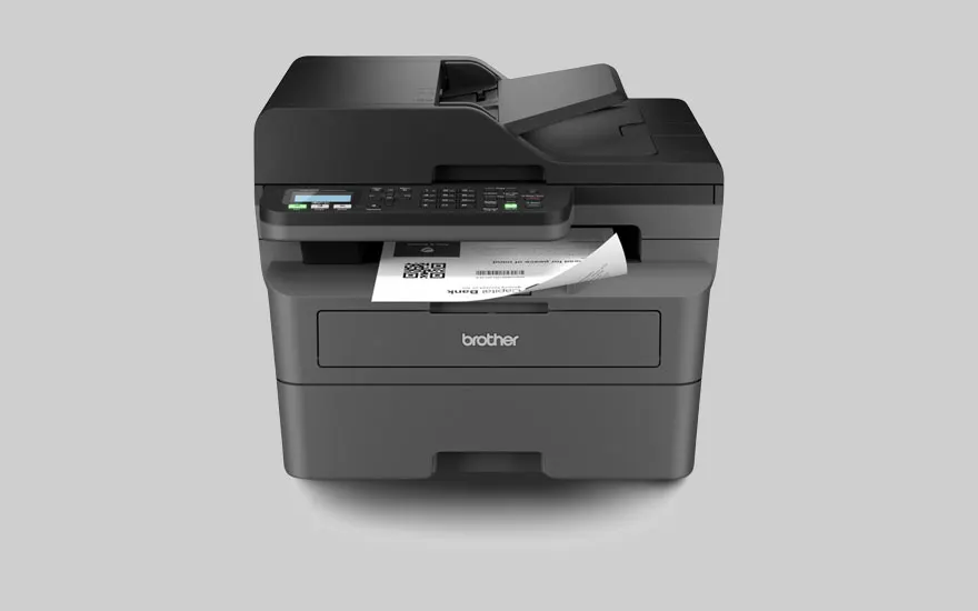 Une imprimante Brother multifonctionnelle noire sur un fond gris clair avec une feuille de papier qui en sort.