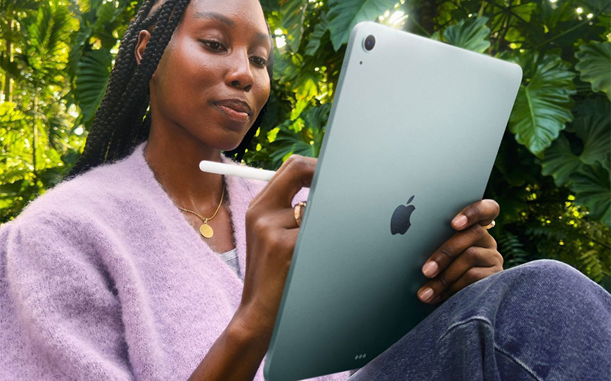 Vrouw in paarse trui houdt groene iPad vast in natuurlijke buitenomgeving. Ontspannen sfeer tussen groene planten en bladeren.