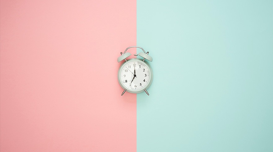 Un réveil blanc est placé au centre, sur un fond divisé verticalement en rose et bleu clair. Les aiguilles indiquent 7h04.