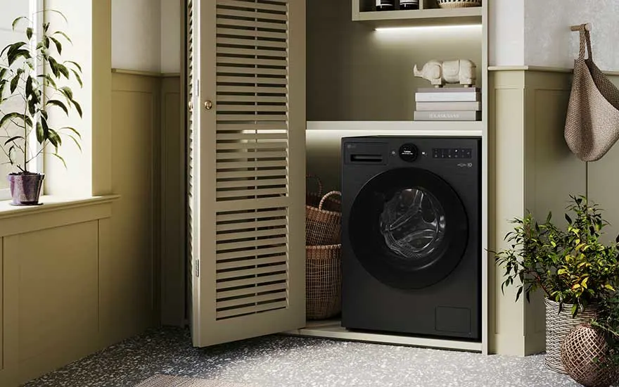 Een zwarte LG wasmachine is elegant geïnstalleerd in een nis van een lichte, uitnodigende ruimte met manden en planten als decor.