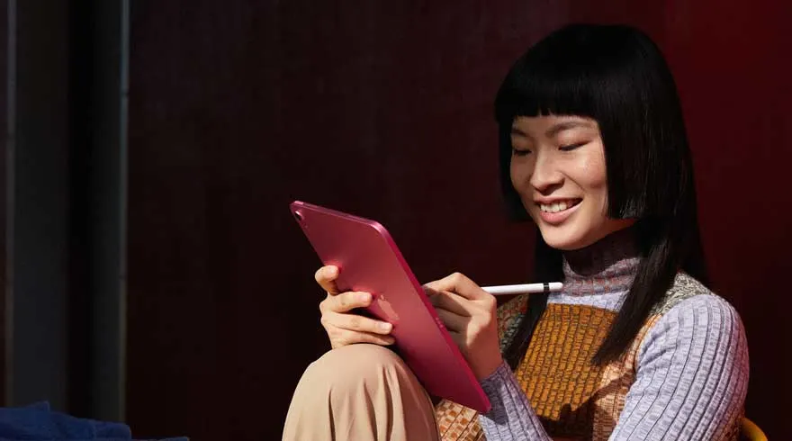 Une tablette rose est tenue et utilisée avec un stylet blanc devant un fond sombre.