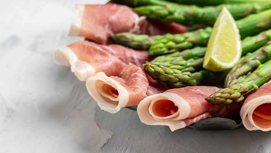 Sur une assiette grise, jambon roulé, asperges vertes et quartier de citron jaune.