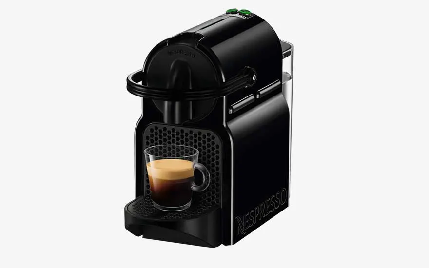A black Nespresso machine prepares an espresso in a transparent cup, featuring two green buttons and a compact, neat design.