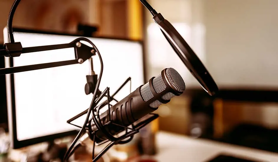 Microphone noir sur support araignée devant écran blanc. Bras articulé et filtre anti-pop visibles.