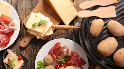 Kaas, vleeswaren en aardappelen op een houten tafel. Kaas ligt op een houten plank. Er zijn ook spatels.