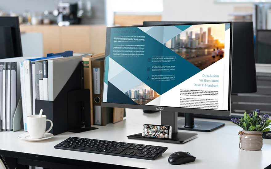 Bureau blanc avec écran d'ordinateur affichant un design graphique bleu et blanc, clavier noir, souris et livres.