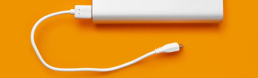 Een witte powerbank ligt op een oranje achtergrond, verbonden met een witte USB-kabel.