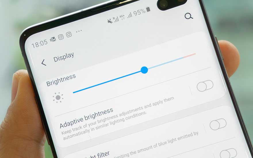 Un téléphone affiche les paramètres d'écran, avec le curseur de luminosité réglable. Les options incluent la luminosité adaptative et le filtre de lumière bleue.