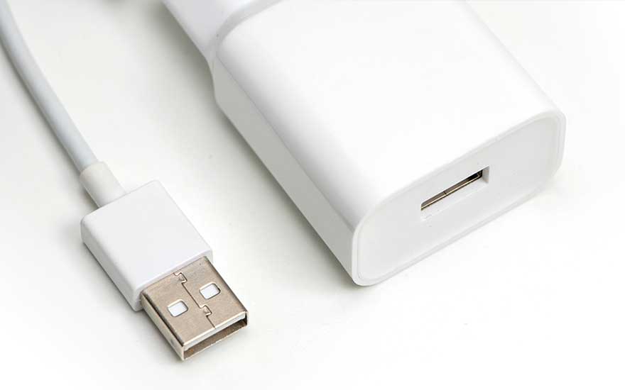 Witte USB-lader en kabel op een witte achtergrond. De lader is rechthoekig met een USB-poort.