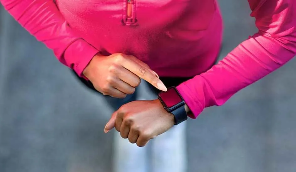 Une personne en chemise rose utilise une montre intelligente noire sur un fond gris uni.