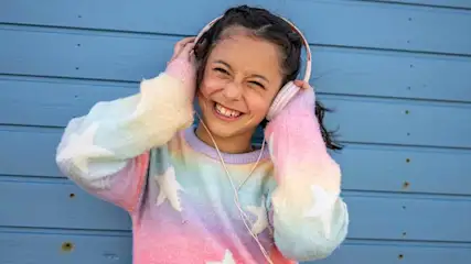 Une personne porte un casque rose devant un mur bleu. Elle porte un pull multicolore avec des étoiles blanches.