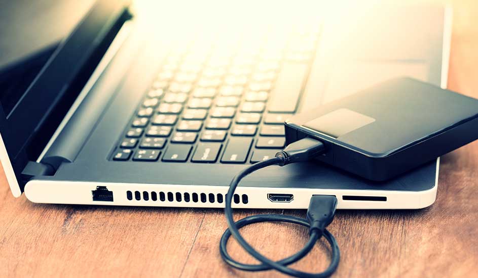 Een open laptop op een houten tafel, met een externe harde schijf aangesloten via een USB-kabel.
