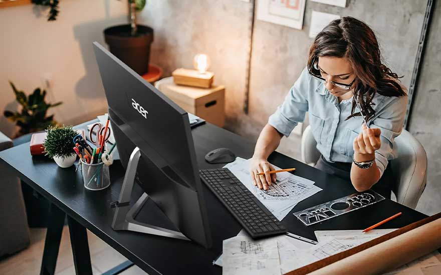 Een zwart bureau met een Acer-monitor, toetsenbord, potloden, en papieren. Een plant en bureaulamp staan op de achtergrond.