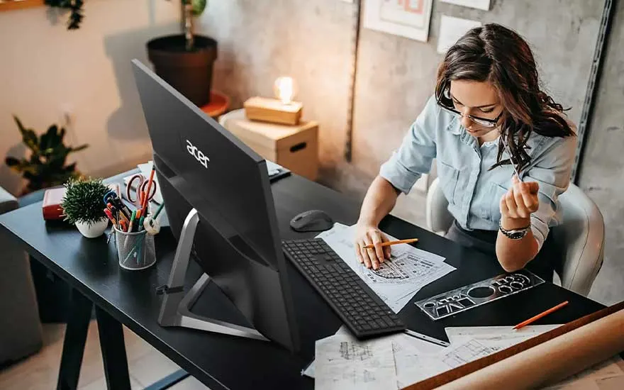 Een zwart bureau met een Acer-monitor, toetsenbord, potloden, en papieren. Een plant en bureaulamp staan op de achtergrond.