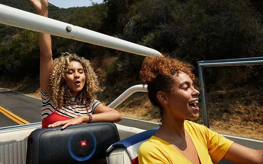 Convertible car with a black JBL speaker. The road and wooded hills are in the background.