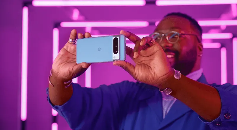 Un téléphone bleu et argenté est tenu devant un fond violet éclairé par des néons.