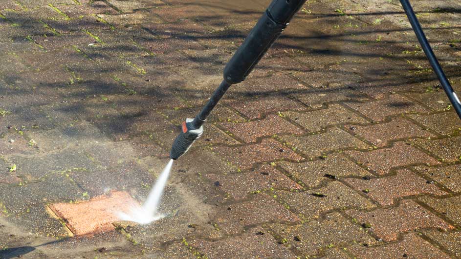 Een hogedrukreiniger spuit water op een stenen terras, waardoor een schoon oppervlak ontstaat.