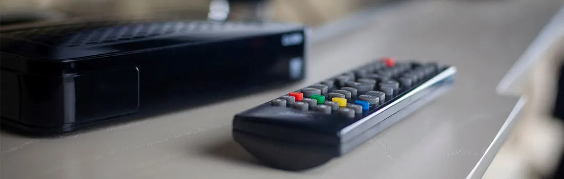 Une boîte noire et une télécommande reposent sur une surface claire. La télécommande a des boutons colorés.